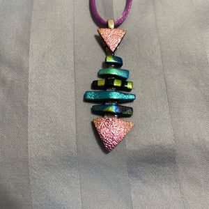 Beautiful fused glass fish in purples and greens on a purple silk cord.